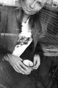 Claire Elizabeth smiling through a coffee shop window in black and white