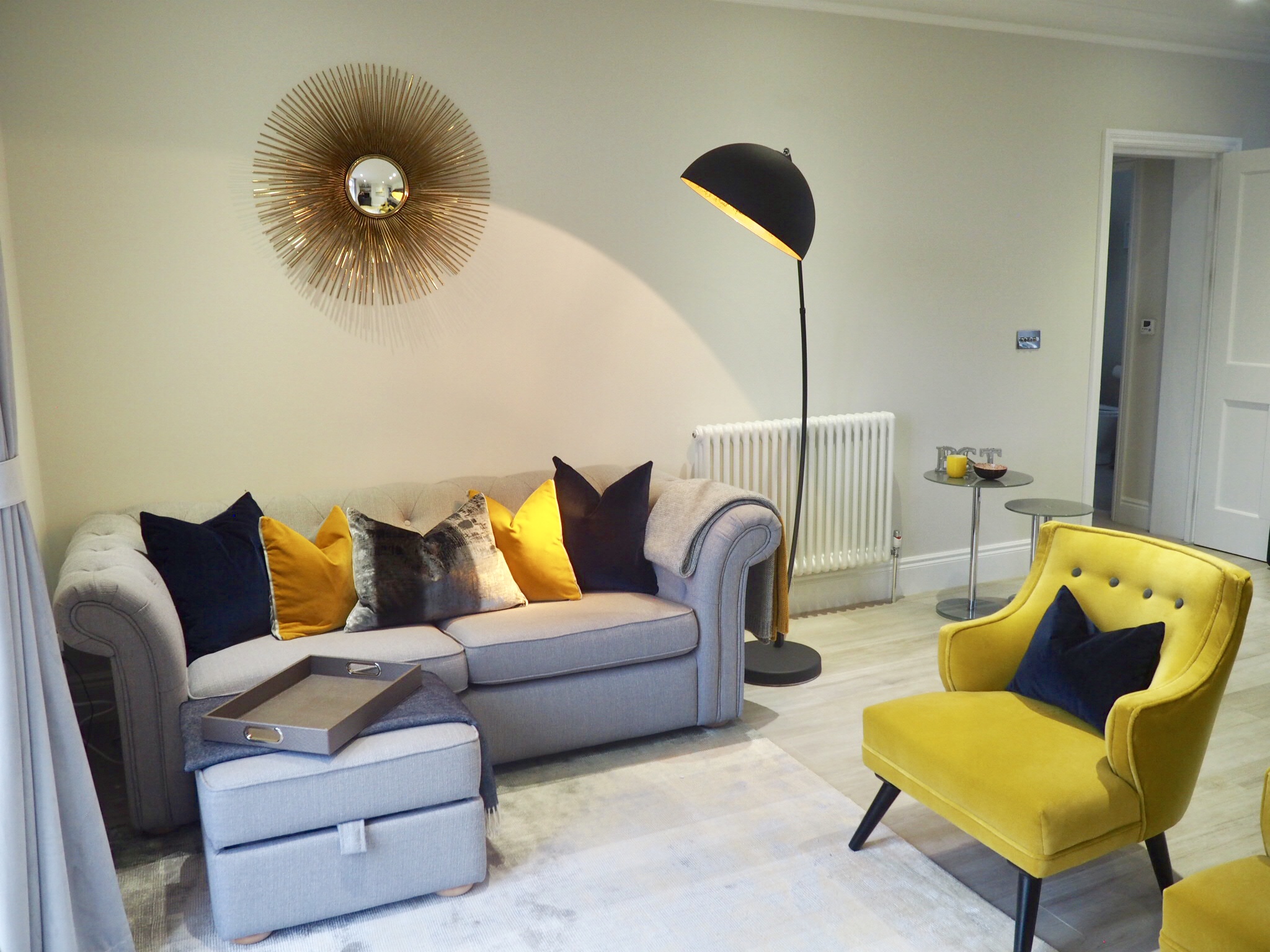 Living room with ombré grey and mustard rug, two mustard coloured chairs and cushions ranging through navy, ochre and grey, with a faux alligator tray.
