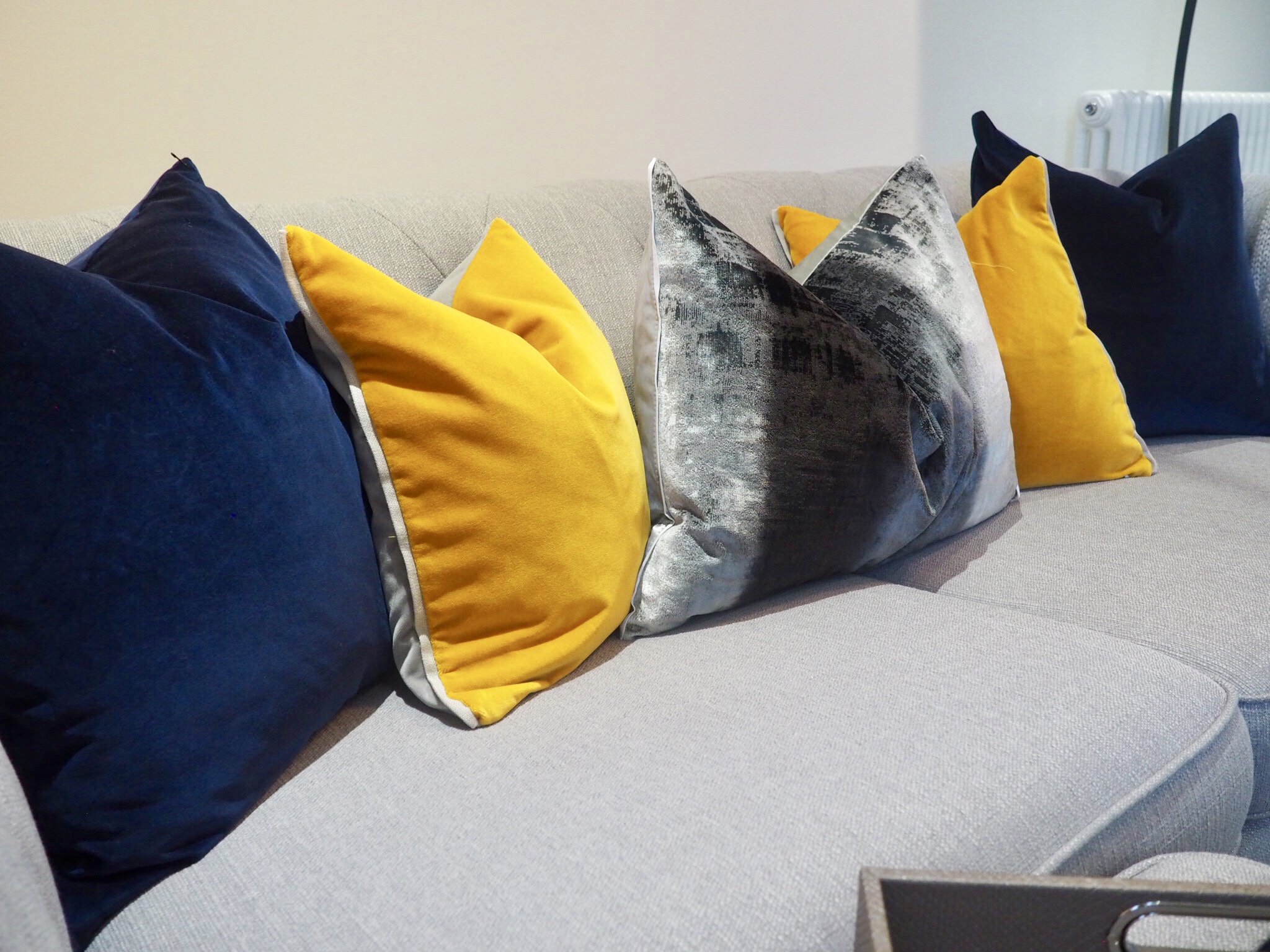 Navy, mustard and grey velvet cushions on top of a grey chesterfield sofa