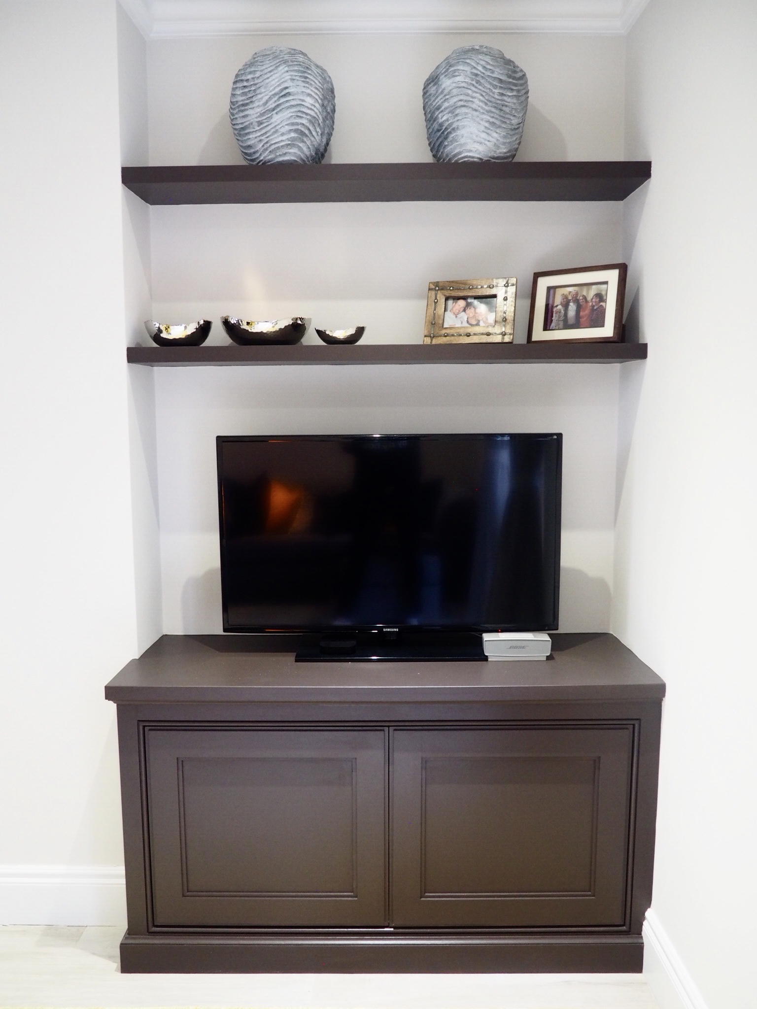 Bespoke media unit with two shelves and silver and copper bowls on the first shelf, and two wavy grey vases on the top shelf