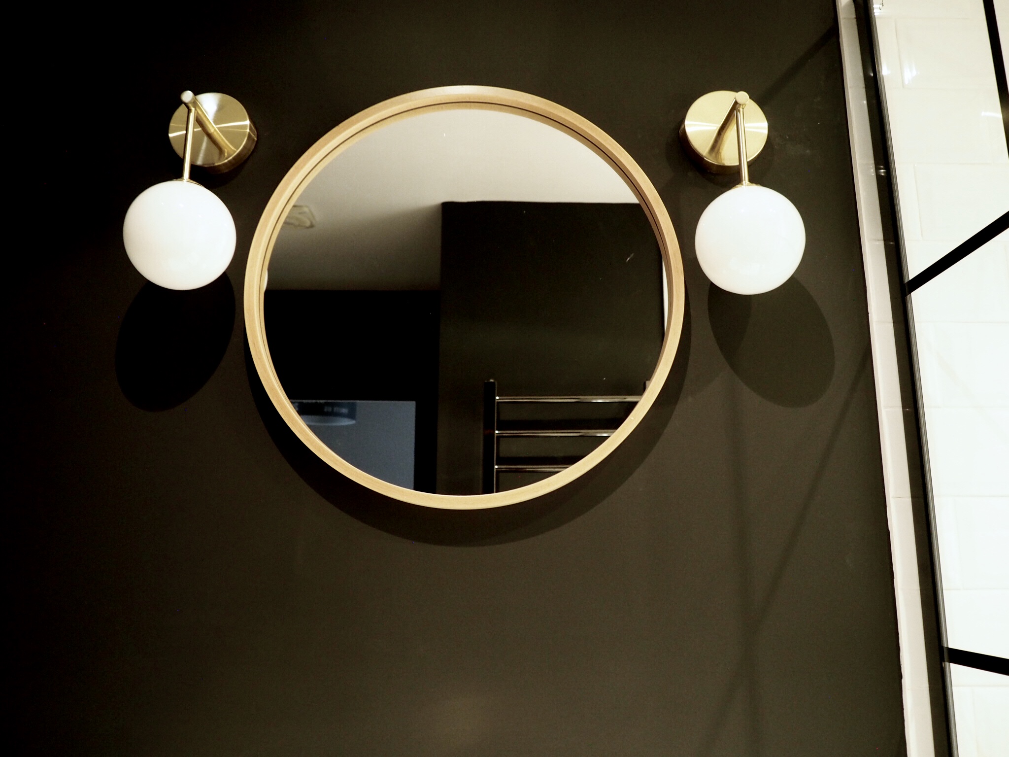 Round wood Zara Home mirror framed by two gold and white wall lights