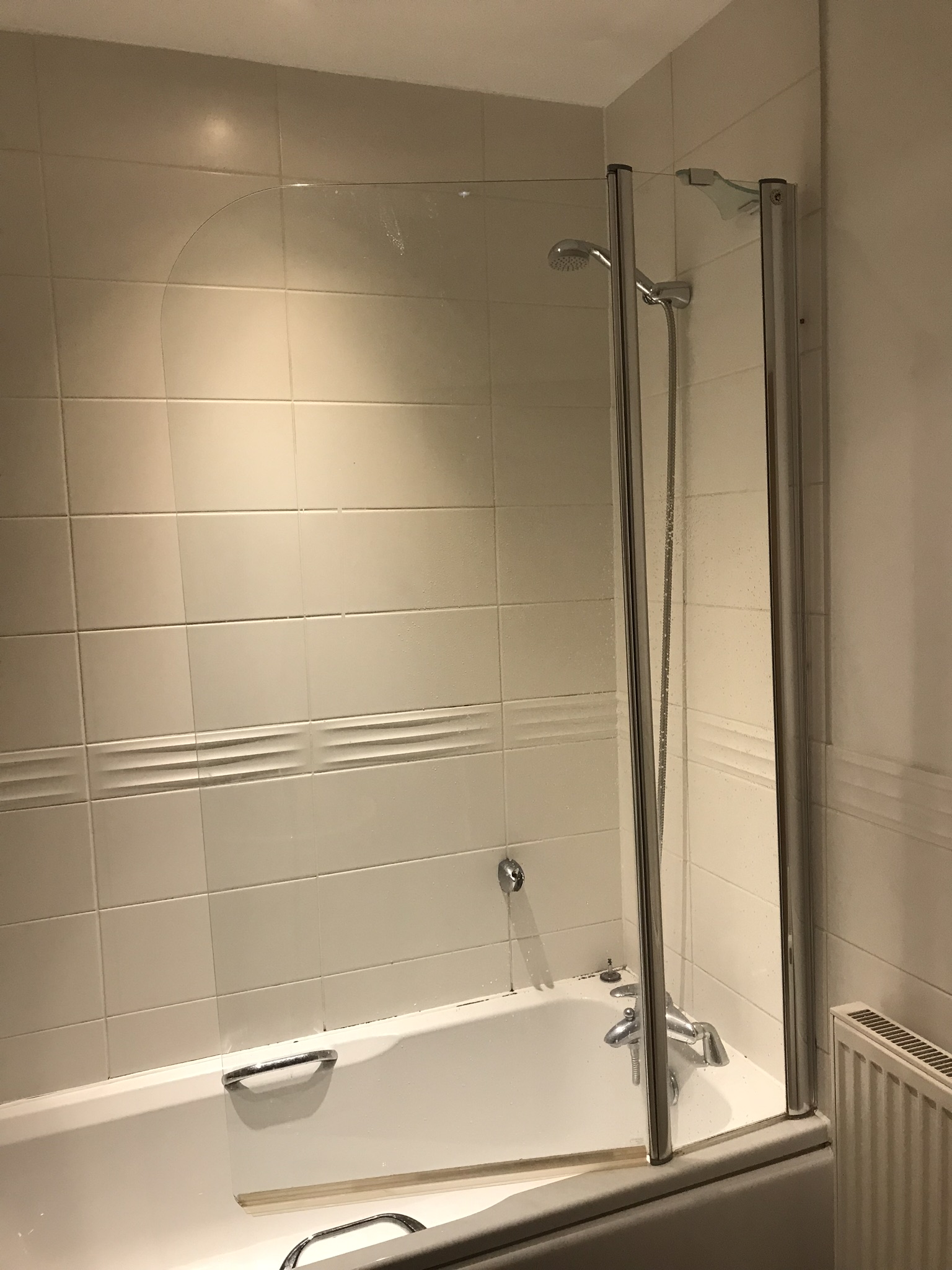 Old bath in the bathroom with shower hose and plain white tiled wall